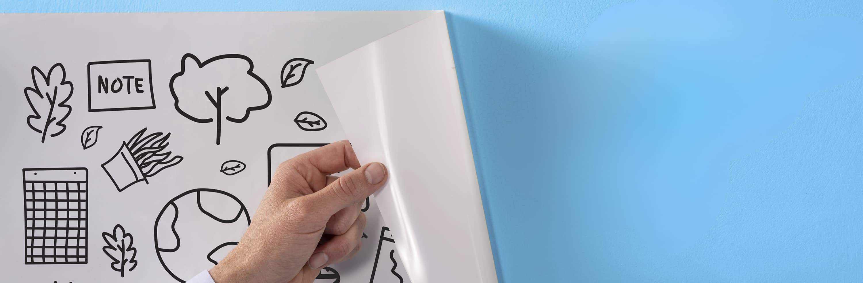 A person peels a transparent whiteboard sheet with doodles off a blue wall. Text reads, "Without traces of glue." An orange cube and the Legamaster Magic-Chart logo are visible.